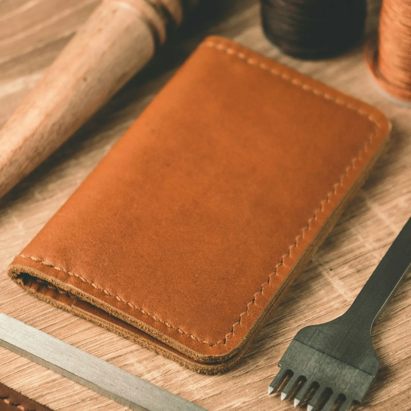 Portefeuille en cuir fauve sur l'établi, à côté d'une griffe de maroquinier