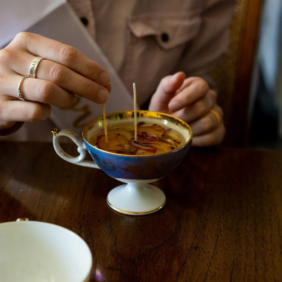 Mains qui fixent une mèche dans une tasse remplie de cire