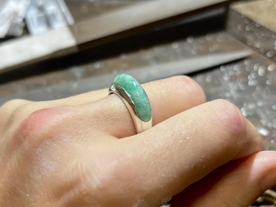Bague à pierre verte portée à la main, dans un atelier