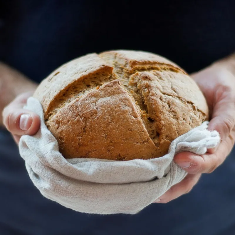 Pain de campagne tout juste sorti du four, tenu dans un torchon