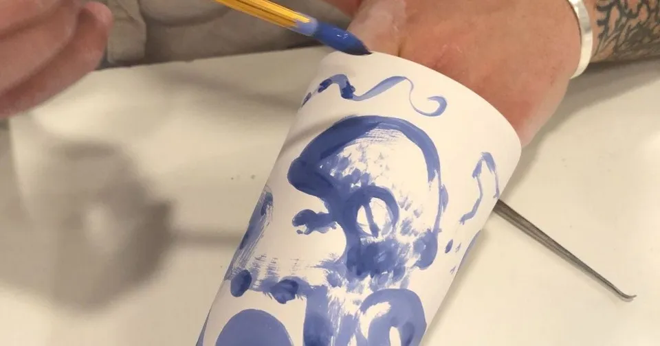 Main qui peint un décor bleu sur une tasse en porcelaine